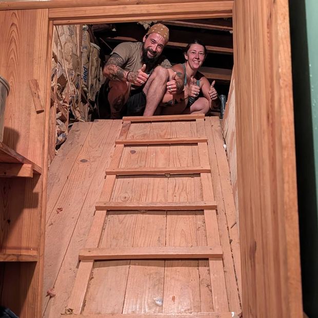 Brad and Jenny giving a thumbs up from inside an attic they are clearing out