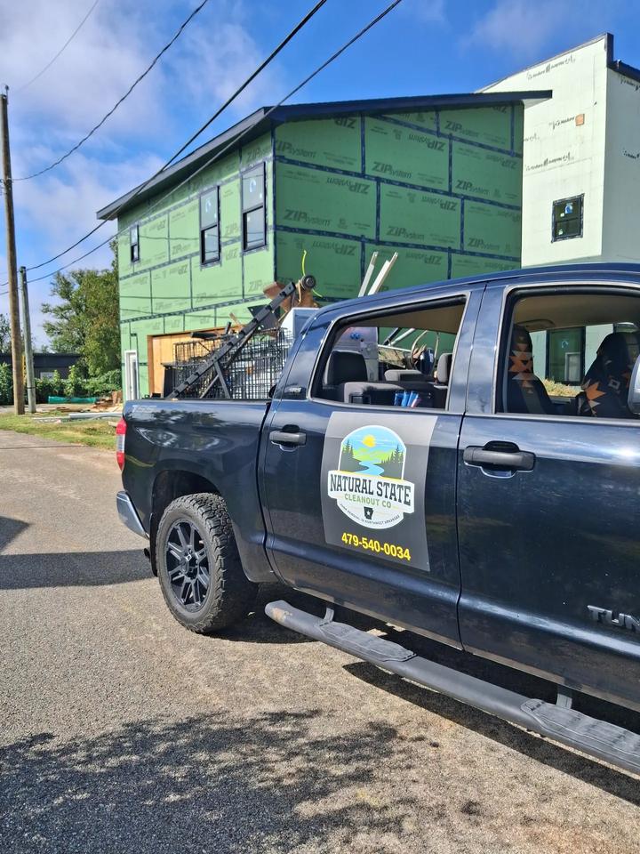 The Natural State Cleanout Co. truck parked at a new-construction job site with a load of debris in the bed